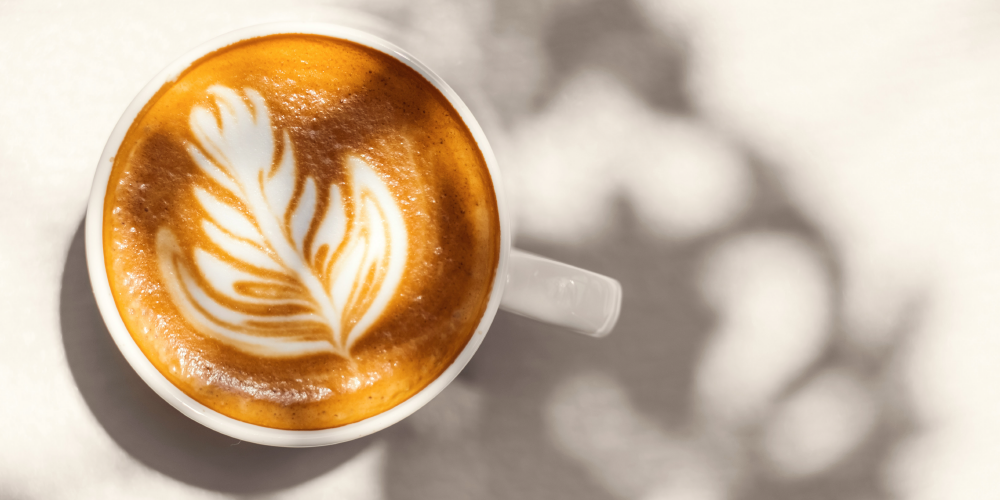 a cup of cappuccino with latteart standing on a white underground
