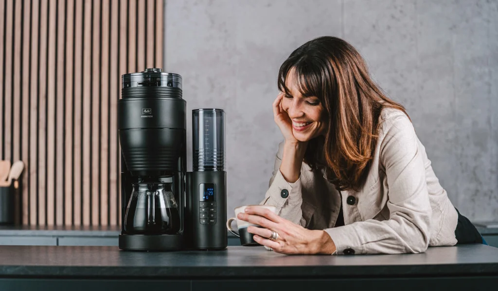 AromaFresh2 in schwarz mit Glaskanne Frau trinkt Kaffee neben einer Melitta AromaFresh