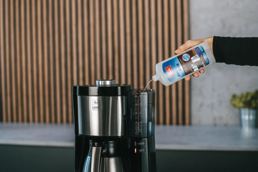 Ung kvinna häller rengöringsmedel i en kaffemaskin.