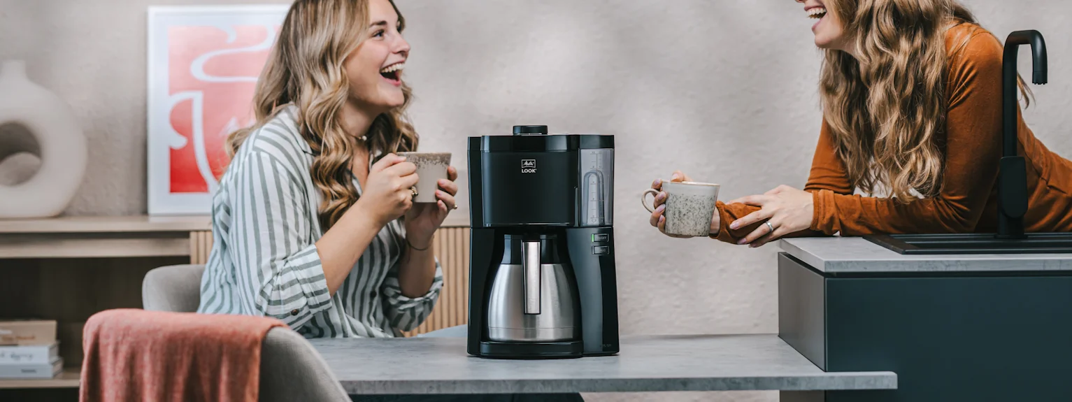 Image of 2 women in a kitchen having coffee from our beautiful Look electric coffee maker which has a thermal carafe.