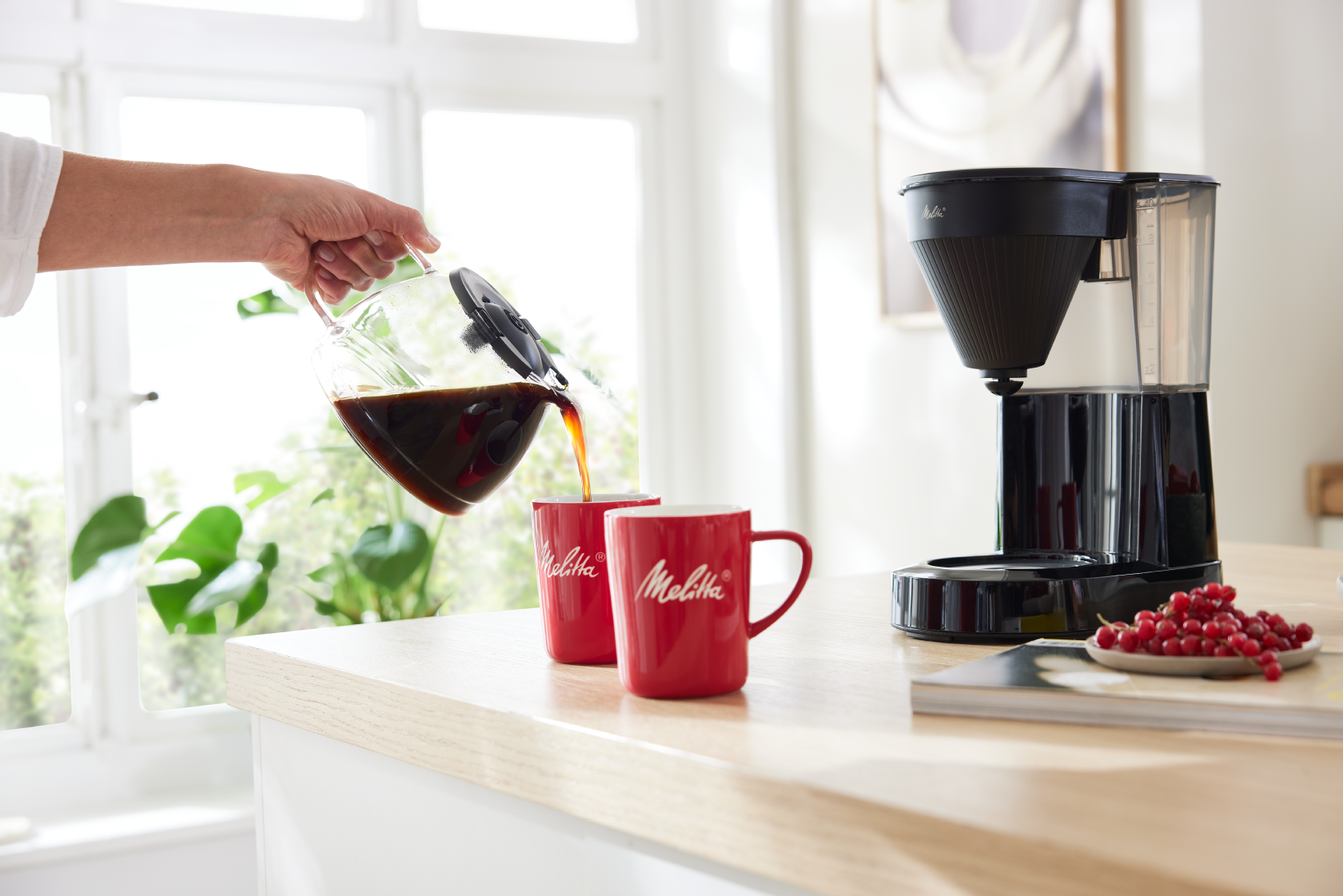 Melitta ®Easy Next Filterkaffeemaschine beim Einschenken von Kaffee in rote Tassen in heller Küche