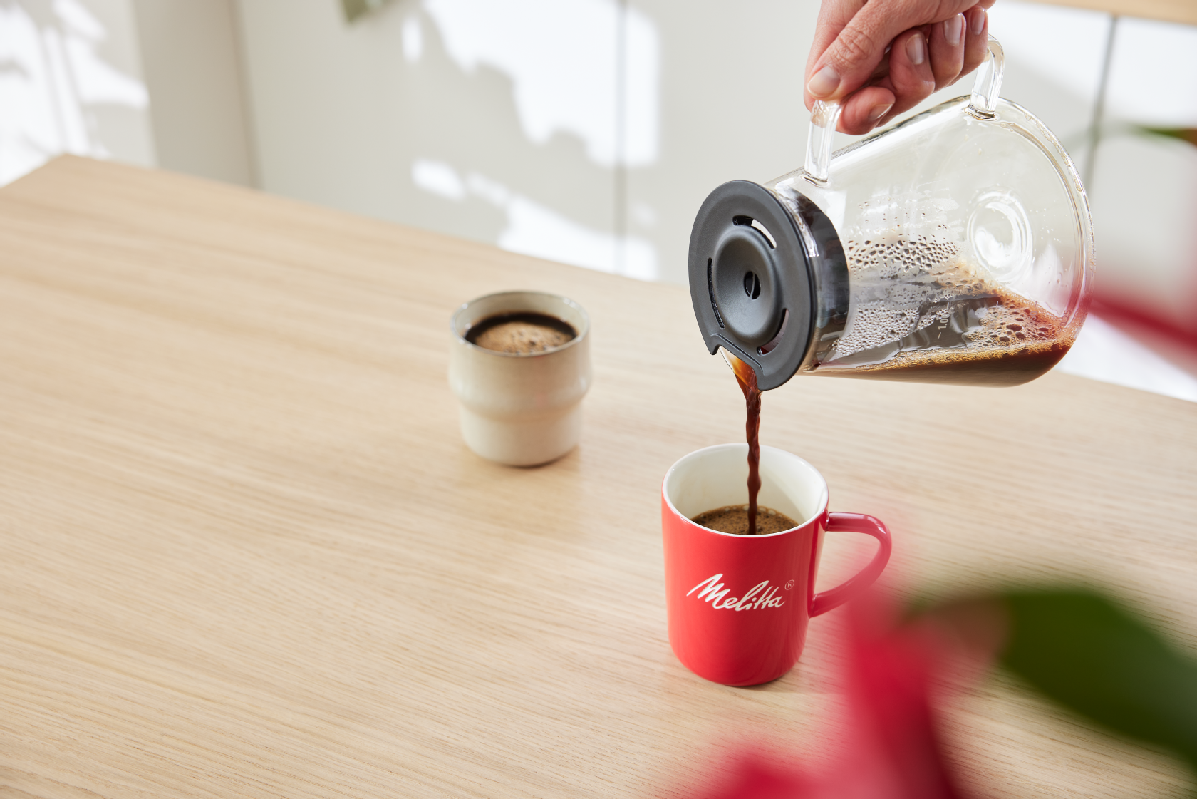 Friskbrygget kaffe hældes fra en glaskande i et rødt Melitta-krus