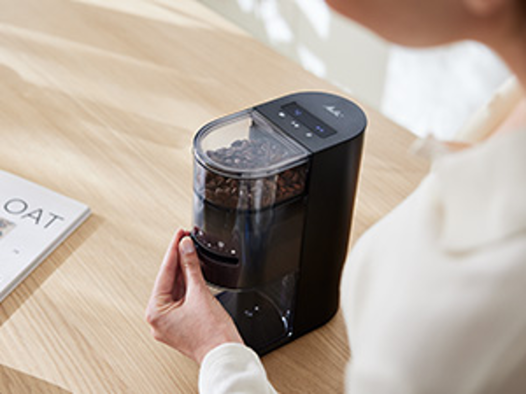 Melitta Linea® Kaffeemühle in Anwendung mit Bohnenbehälter und digitalem Bedienfeld auf Holztisch.