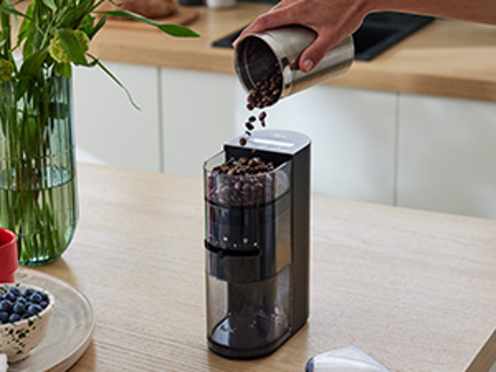 Hand füllt Kaffeebohnen in die Melitta Linea® Kaffeemühle auf einer Küchenarbeitsplatte.