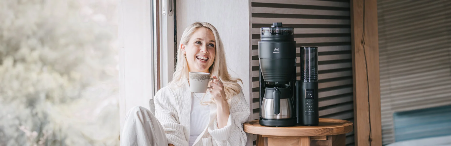 Frau genießt Kaffee neben Melitta AromaFresh Pro Filterkaffeemaschine auf einem Holztisch.