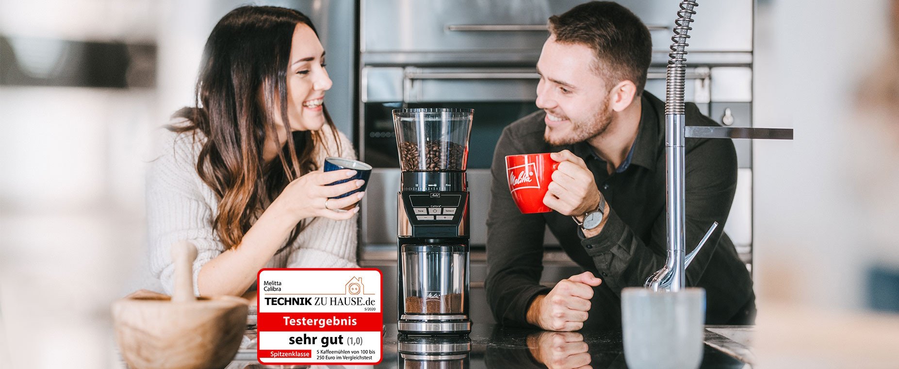 Two Models drinking coffee, between a Melitta Calibra and the logo of "Technik zu Hause"