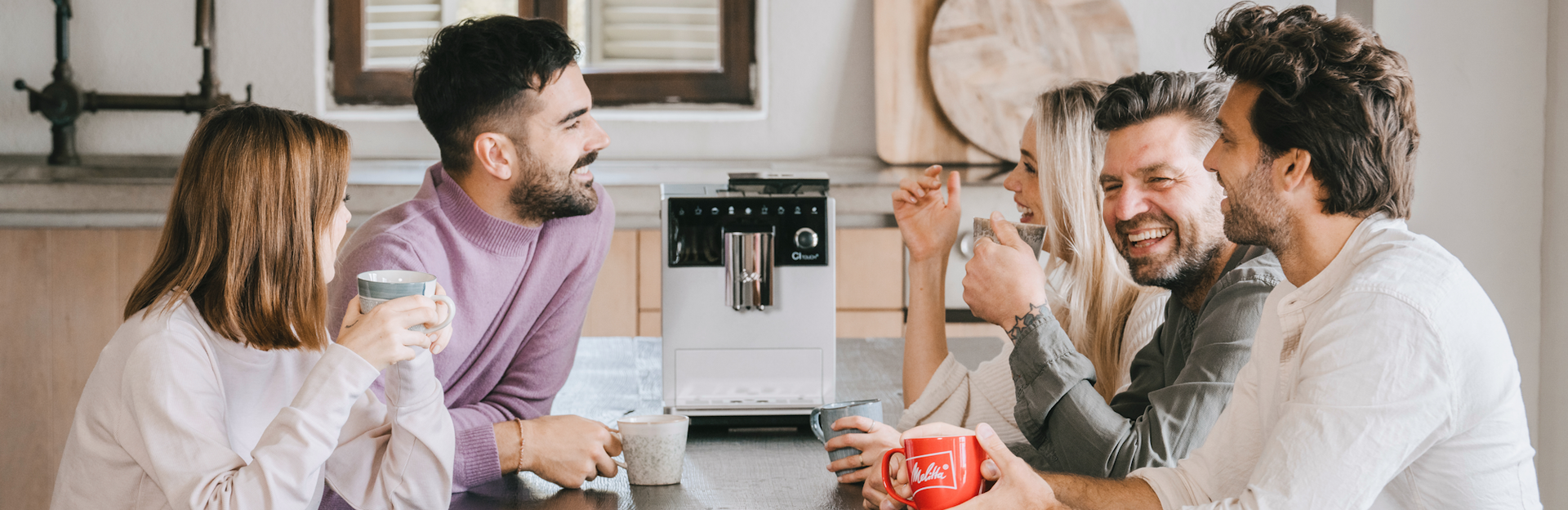 Group of friends enjoying coffee with a white Melitta CI Touch coffee machine on the table