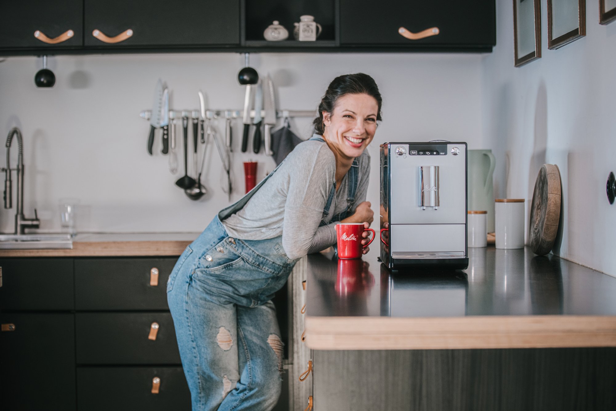 Frau lehnt mit Kaffee an Küchentresen neben einem Melitta Vollautomaten.