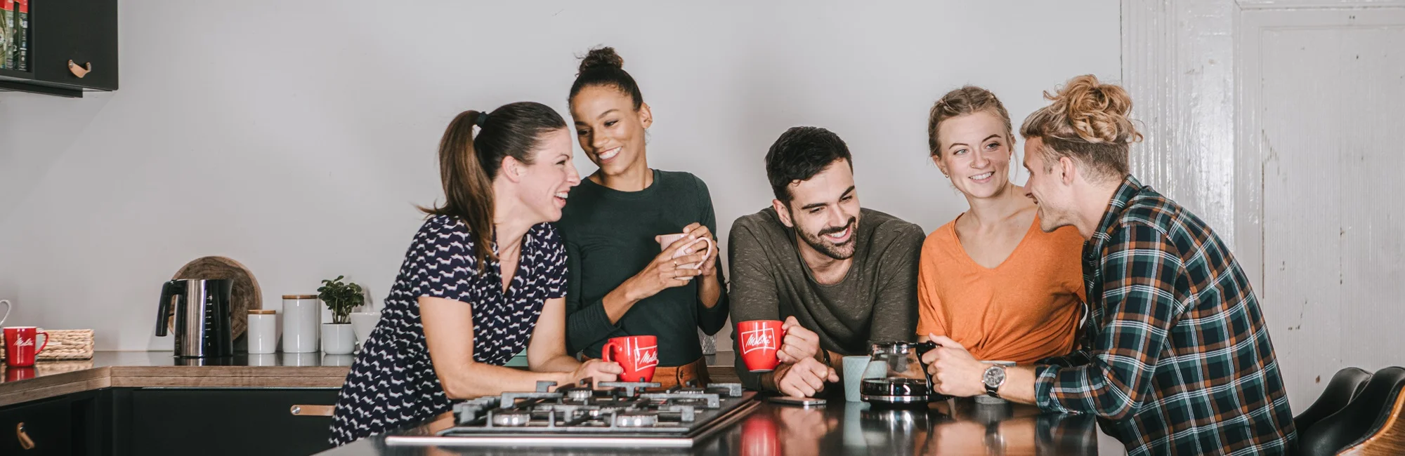 Melitta Genuss Fünf Models stehen an einem Tisch, unterhalten sich und trinken einen Melitta Kaffee.