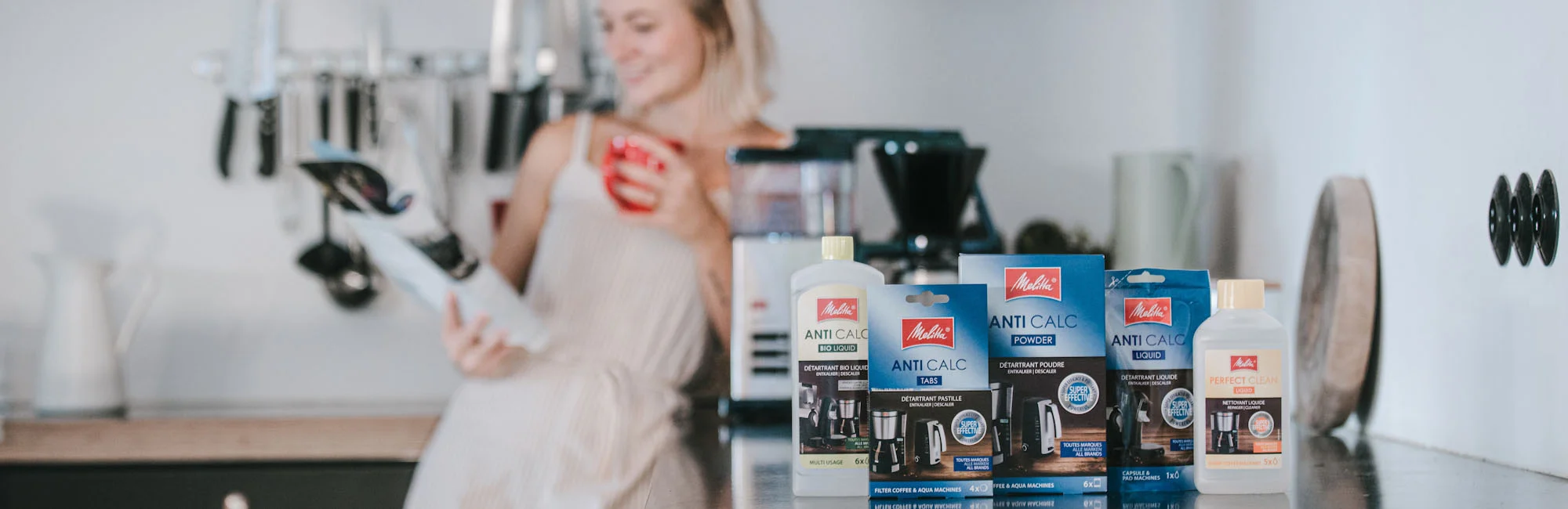 Image of a woman in a kitchen drinking coffee from a coffee maker from our range of electric coffee makers. Our range of descalers is featured on the front page.