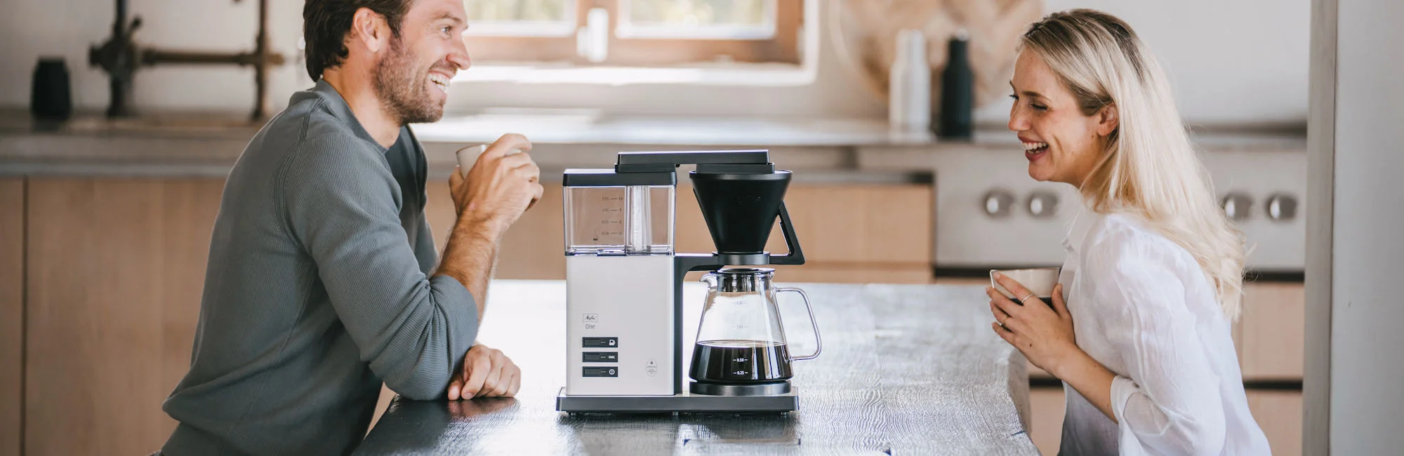 Image d'un couple assis à table prenant un café dans leur cuisine moderne avec l'une de nos cafetieres en presentation sur leur plan de table