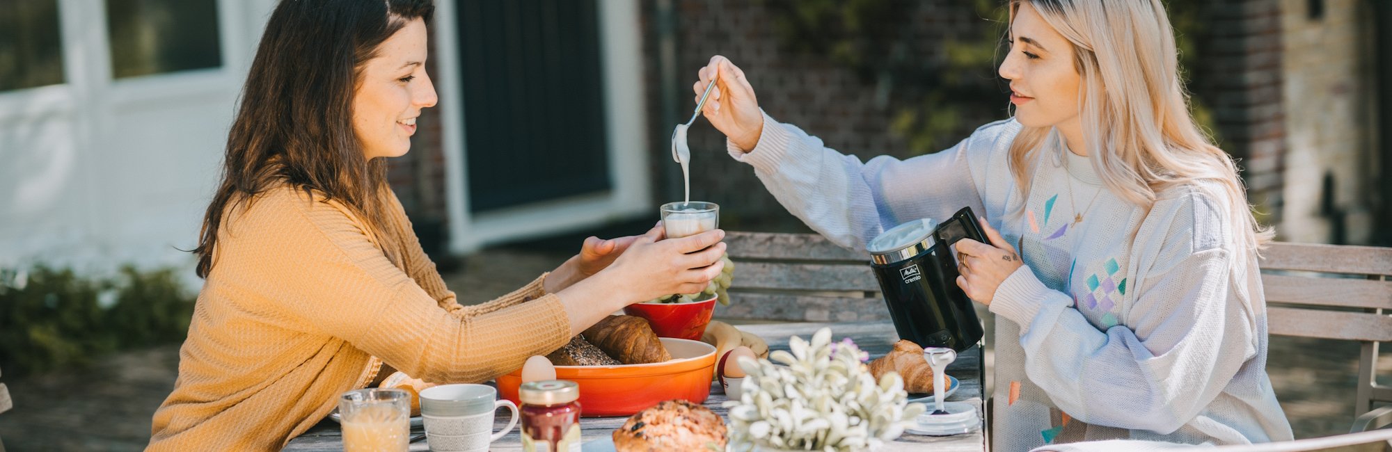 Zwei Frauen trinken Latte Macchiato auf der Terasse und verwenden einen Melitta Milchaufschäumer