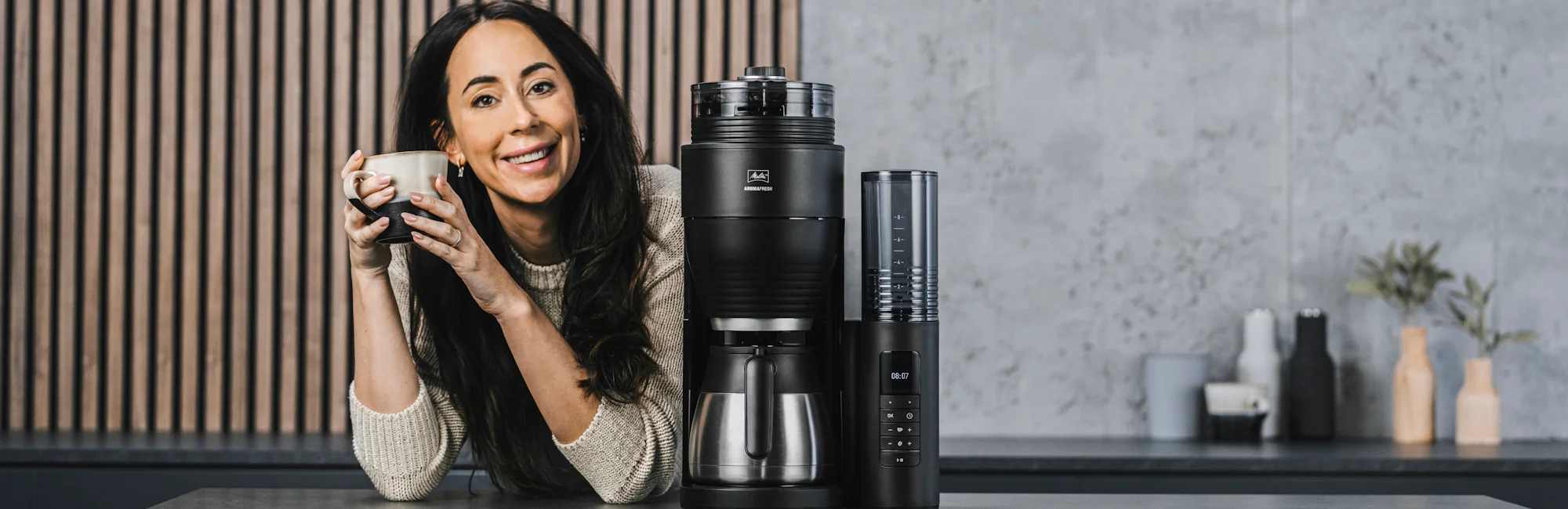 A woman drinks a cup of Melitta coffee next to a Melitta Aromafresh thermal coffee machine