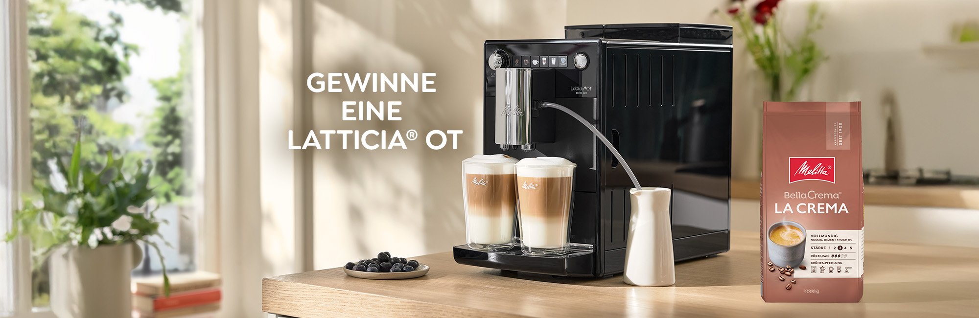 Latticia® OT steht auf der Kuchenzeile mit zwei Latte Macchiato und einer PackungMelitta® BellaCrema® La Crema Kaffeebohnen