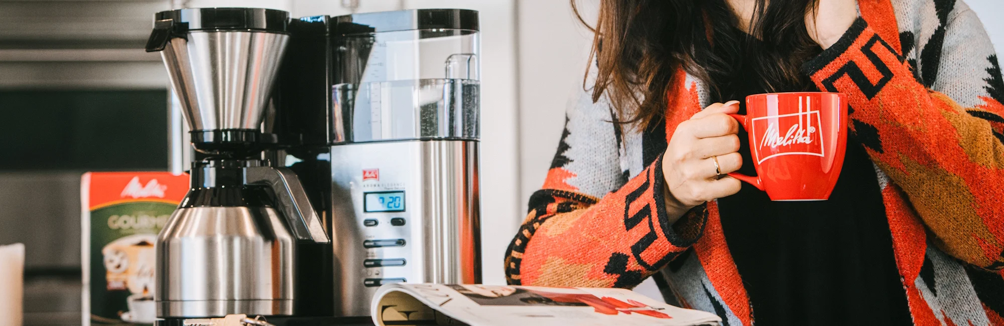 een vrouw drinkt een Melitta koffie naast een Melitta koffiemachine