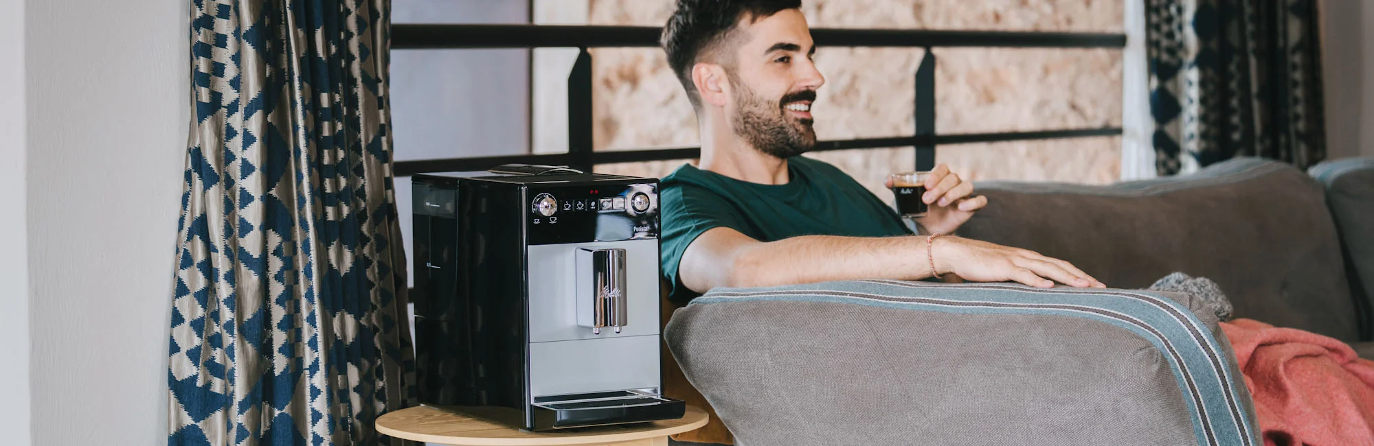  Image of a handsome smiling man sitting on his sofa enjoying an espresso