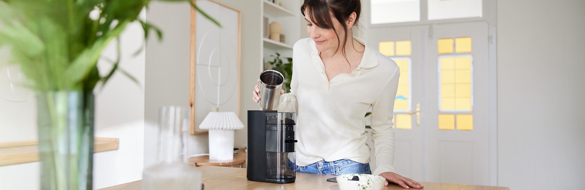 Frau befüllt die schwarze Melitta Linea® Kaffeemühle mit Kaffeebohnen.