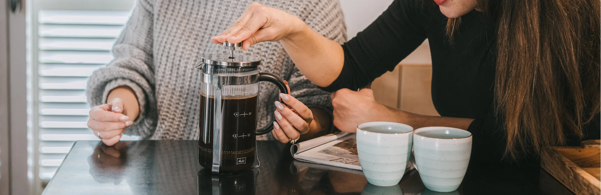 Vrouw drukt met haar hand koffie in de French Press, ernaast staan ​​twee kopjes