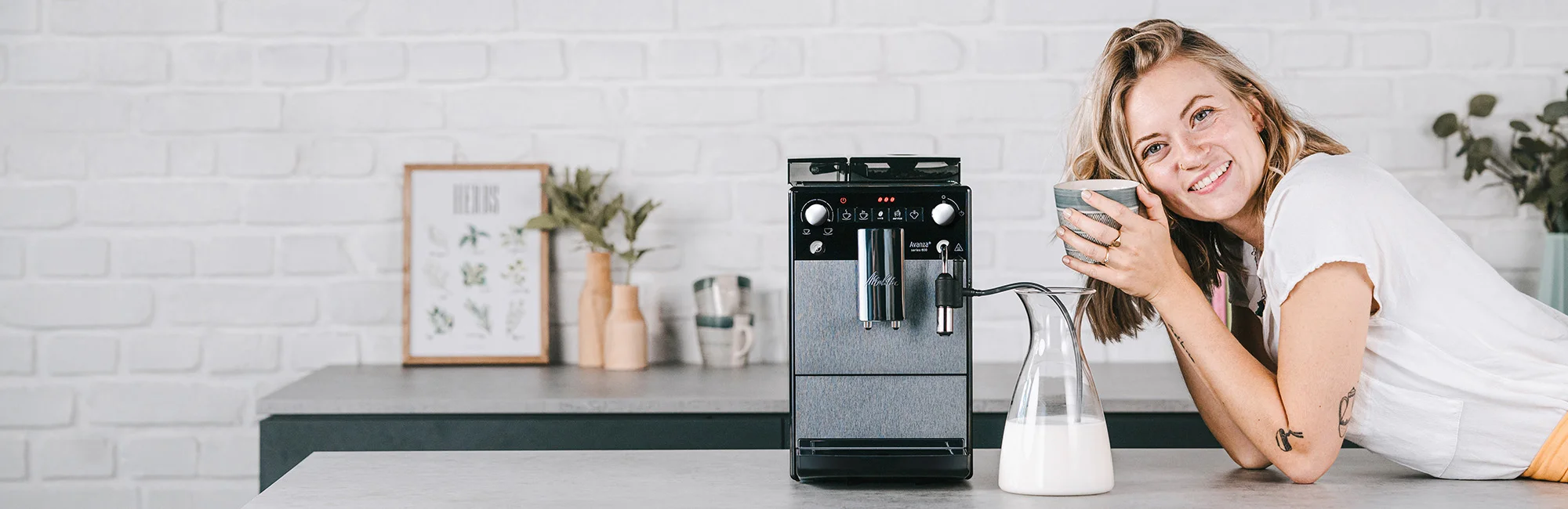 Frau in der Küche steht neben dem Melitta Avanza Kaffeevollautomaten und genießt ihren Kaffee.