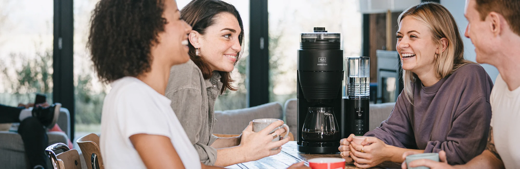 Group of friends enjoying coffee around a table with a black Melitta filter coffee machine with thermal jug