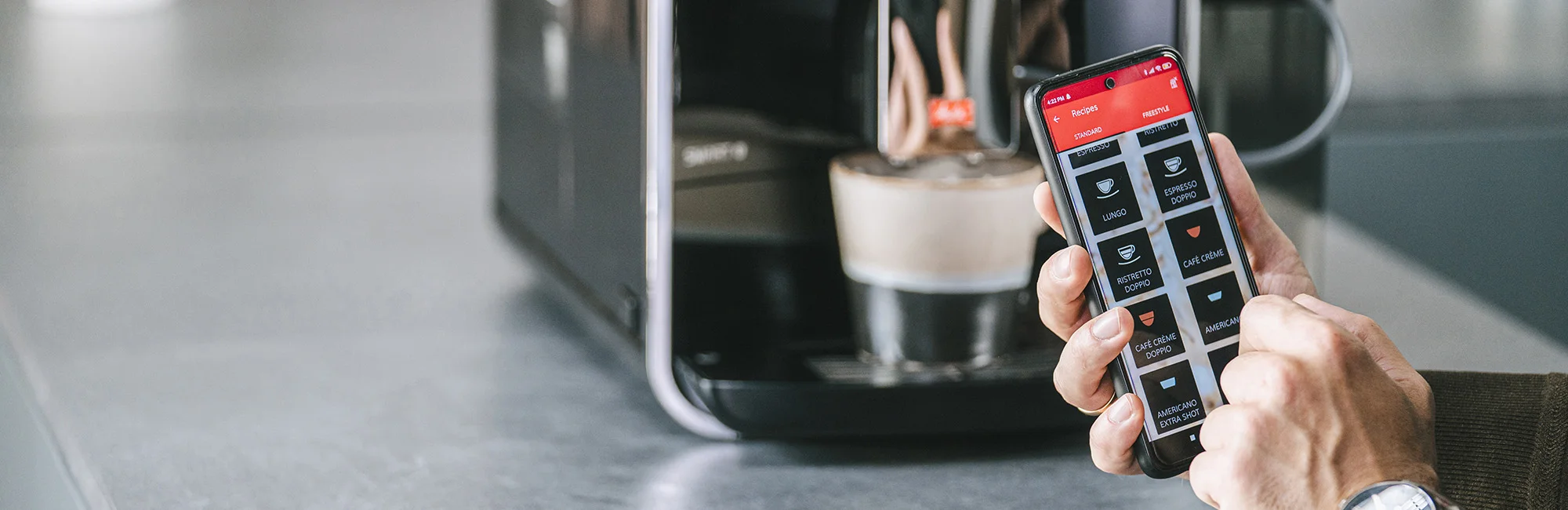 Nutzer wählt ein Kaffeegetränk über die Melitta App neben einer verbundenen Kaffeemaschine