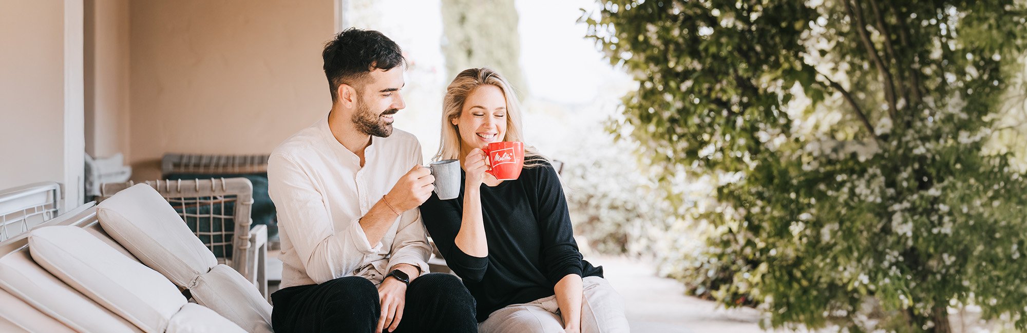 Paar sitzt auf der Terasse auf einer Liege und trinkt einen Kaffee