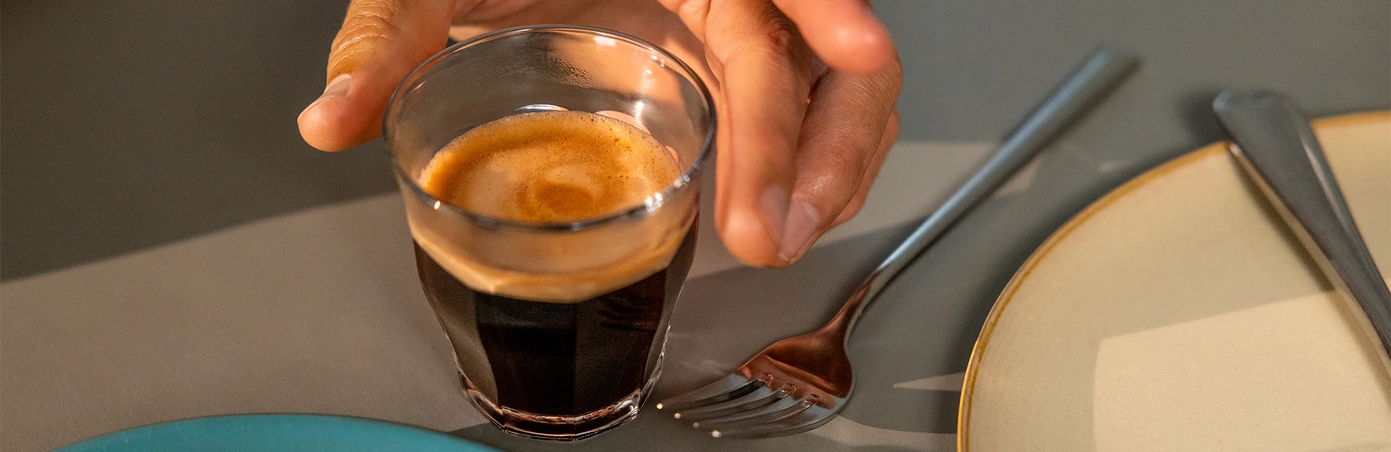Ein Espresso oder Café Crema in einem durchsichtigen Glas und eine Hand, die danach greift
