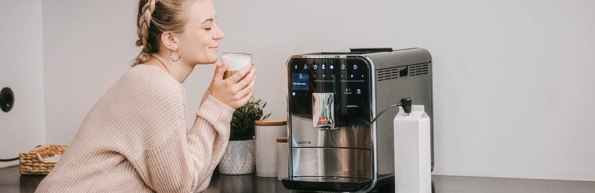 A woman drinks a Latte Macciato in front of a Melitta Barista fully automatic machine