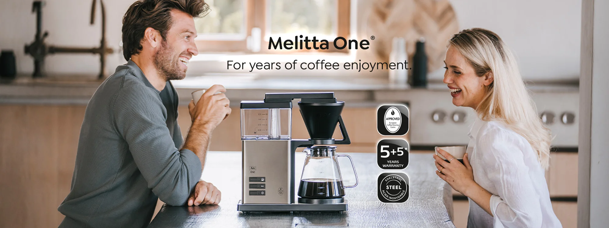 Två personer sitter vid ett bord och njuter av sitt kaffe från Melitta One filterkaffemaskinen.