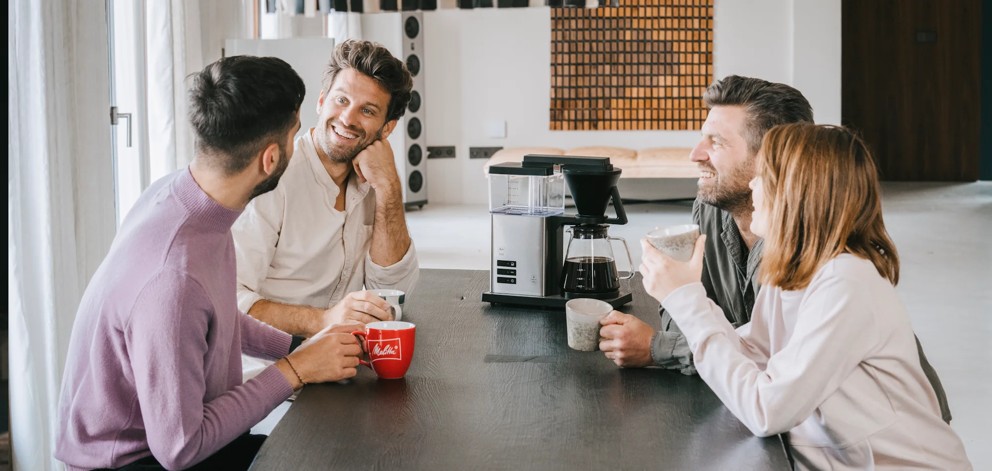 Melitta One Quatre personnes sont assises autour d'une table et savourent un café préparé avec la cafetière filtre Melitta One.