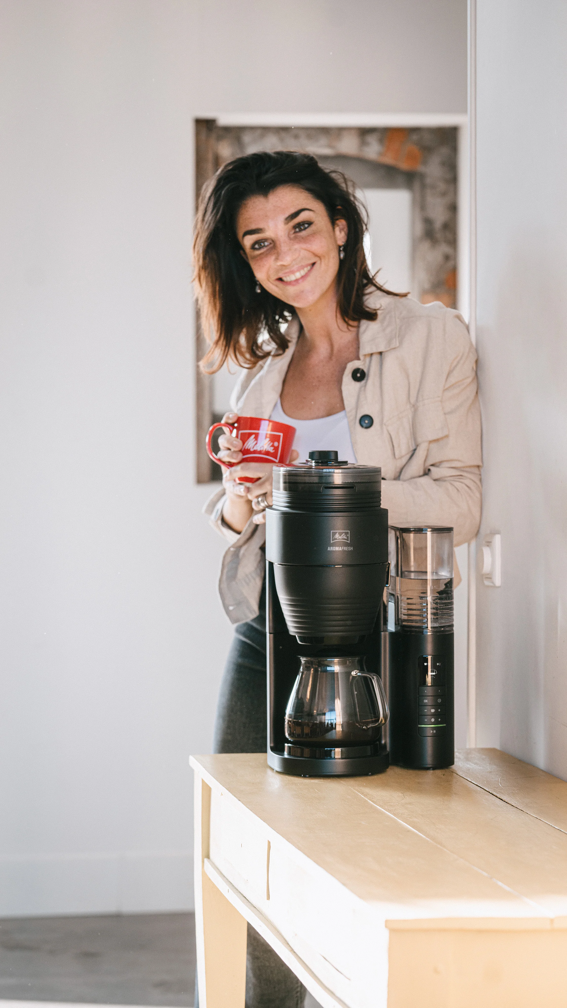 Frau mit roter Melitta-Tasse neben AromaFresh Pro Filterkaffeemaschine auf Holztisch