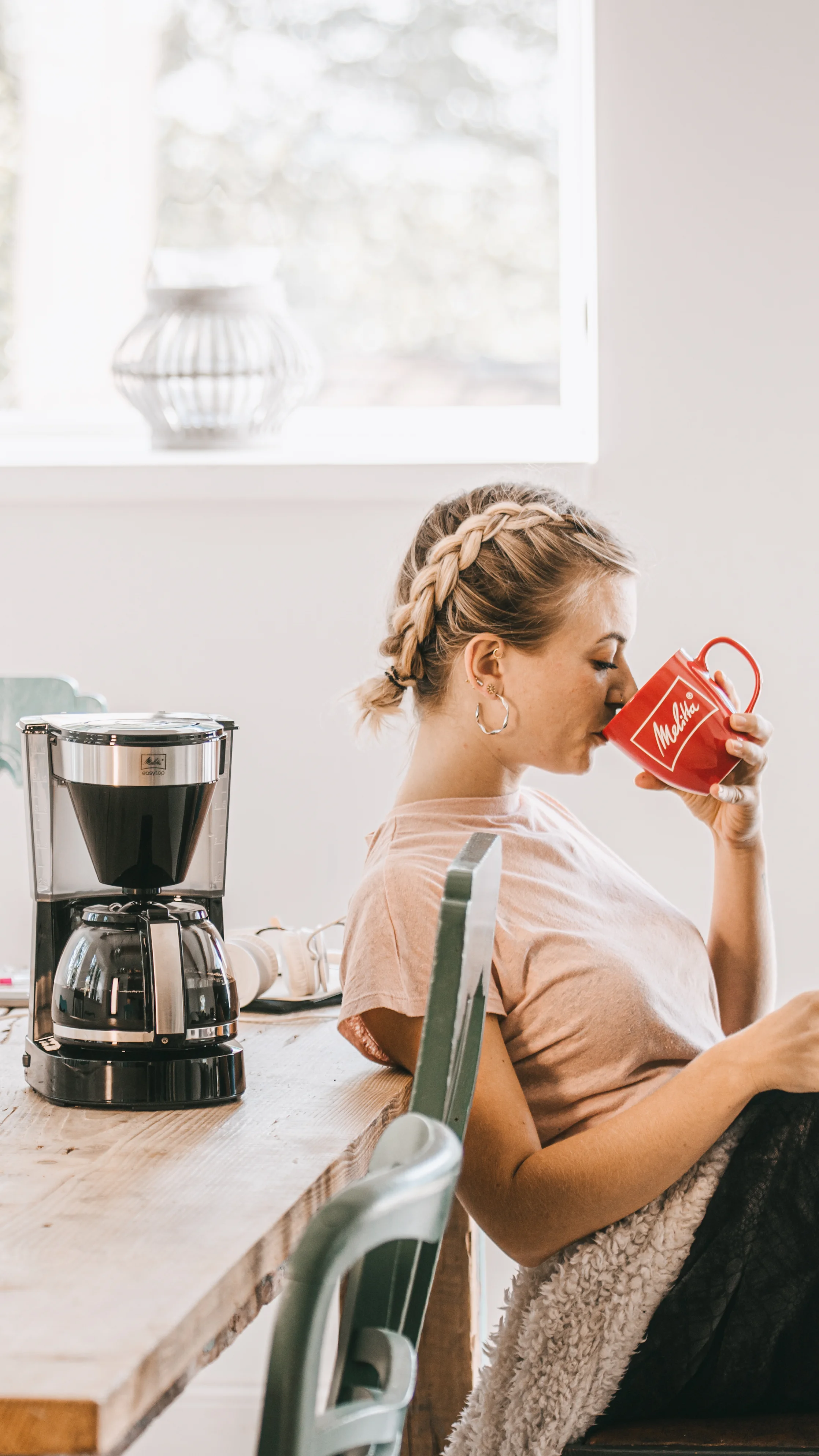 Kvinde nyder kaffe fra en rød Melitta-kop ved siden af en sort Melitta Easy Top filterkaffemaskine
