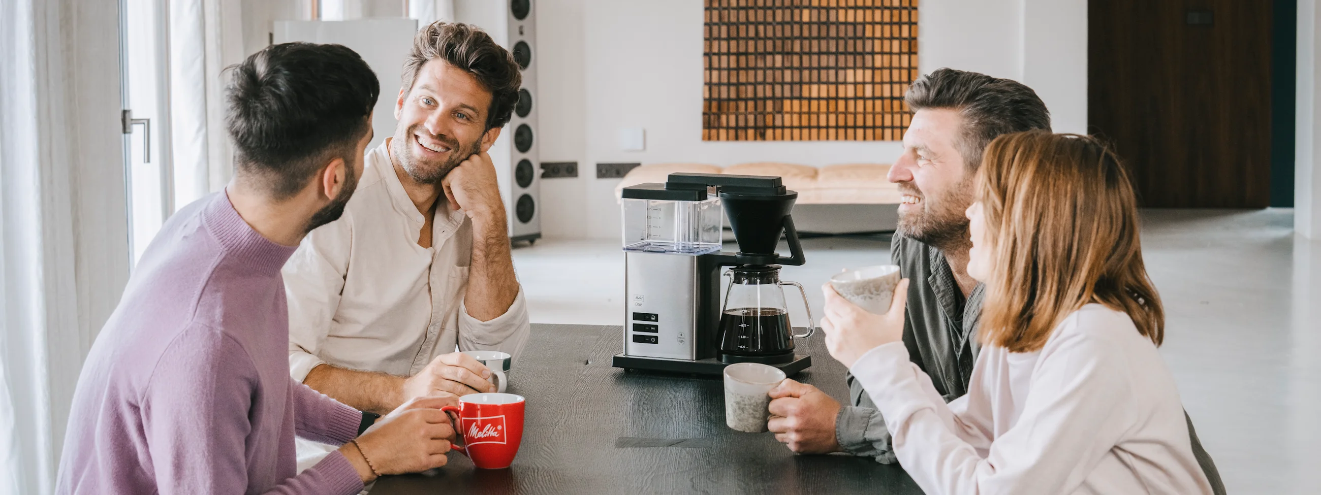 Fyra personer sitter vid ett bord och njuter av kaffe från Melitta One filterkaffemaskinen.