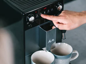 En modell gör sig en kopp Melitta-kaffe med en Melitta helautomatisk kaffemaskin.
