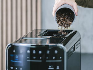 Mano vertiendo granos de café en la cafetera Melitta Barista T Smart