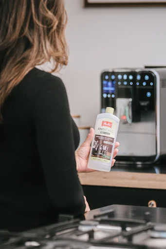 Image of a woman preparing to descale her automatic machine with liquid descaler