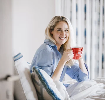 Lächelnde Frau mit roter Melitta Tasse beim Kaffeegenuss auf dem Sofa