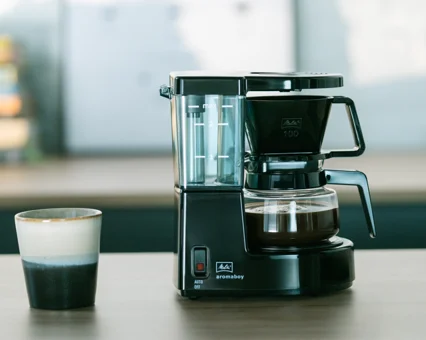 Melitta Aromaboy i sort med glaskande og keramikkop på træbord.