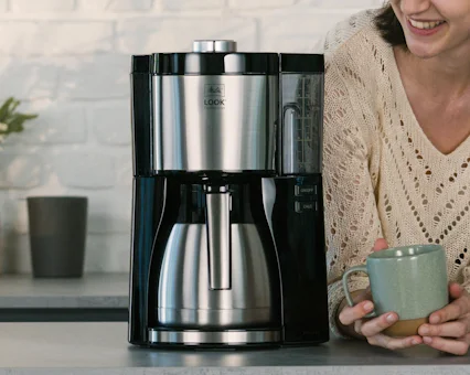 Melitta Look V Therm Perfection con jarra de acero junto a mujer sonriente con taza.
