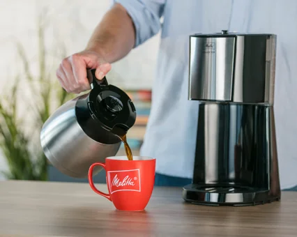 Cafetière Melitta Enjoy Top Therm avec café versé dans une tasse rouge.