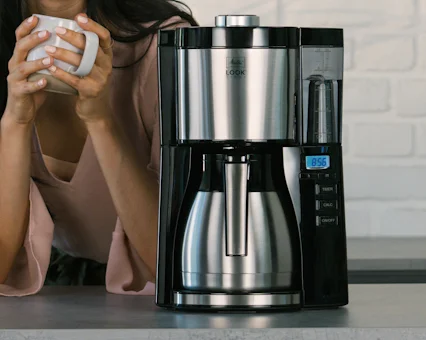 Melitta Look Therm Timer con jarra térmica y pantalla digital, persona sosteniendo taza.