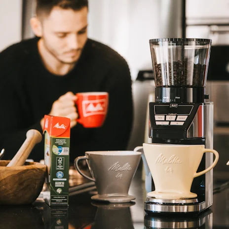 Melitta Calibra bonen maler met op achtergrond iemand die koffie drinkt
