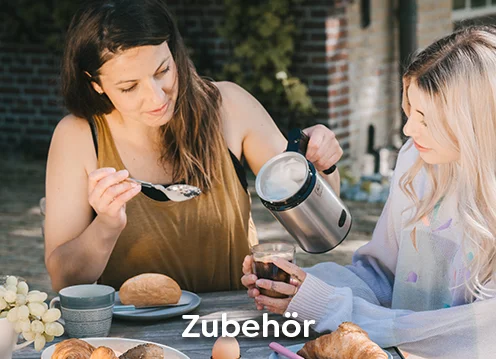  Zwei Frauen sitzen an einem Tisch und bedienen dabei den Melitta Cremio Milchaufschäumer