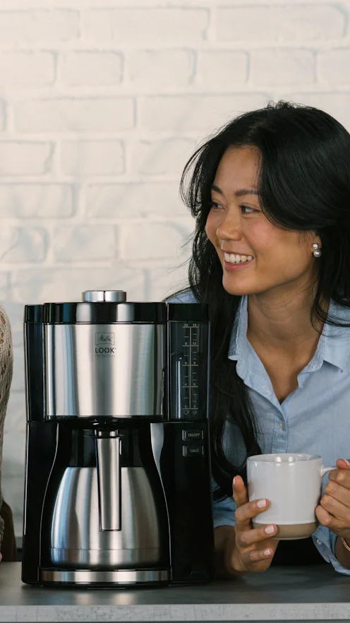 Melitta Look V Therm Perfection con jarra de acero delante de mujer sonriente con taza.