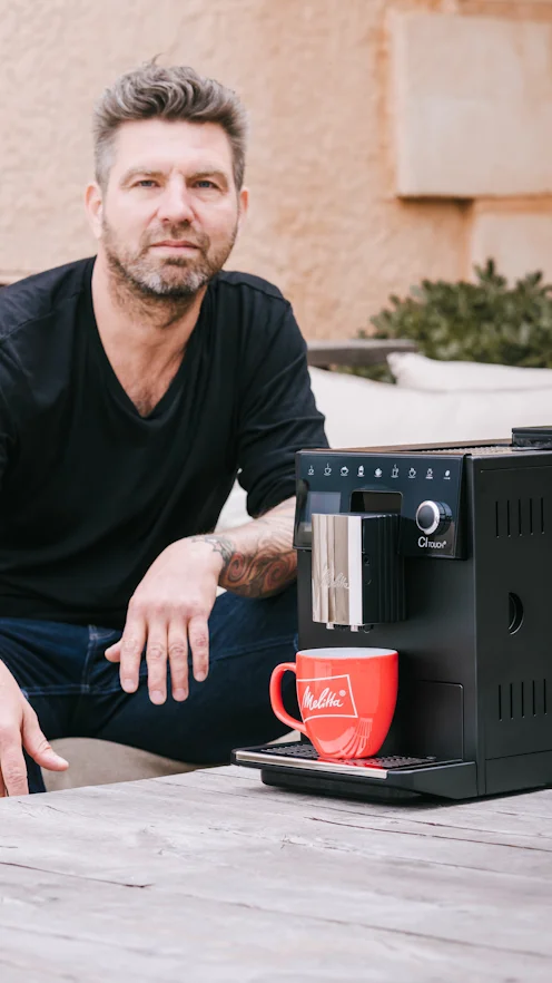 Mann sitzt draussen neben einer Melitta CI Touch mit roter Melitta Tasse