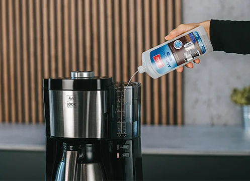 Jeune femme verse du nettoyant dans une machine à café.