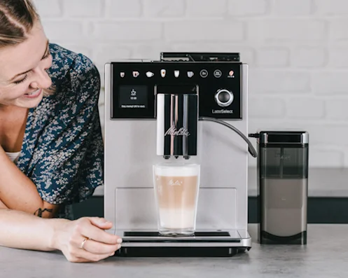 Image of a smiling woman in front of her freshly brewed coffee made with our Latte Select machine.