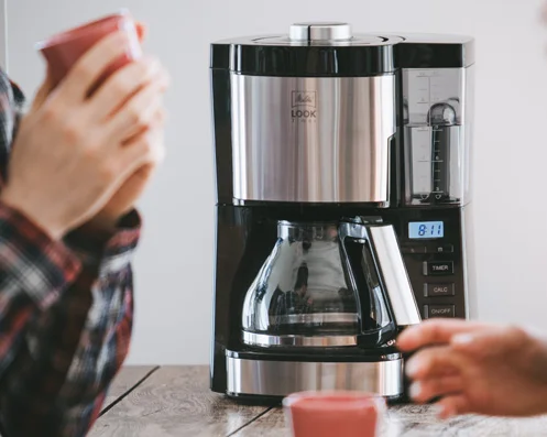 Melitta Look Glaskanne Timer auf Tisch zwischen Personen, digitale Uhr zeigt 8:11.