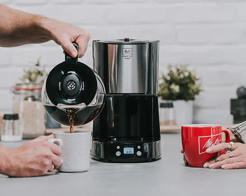 Un hombre vierte café Melitta de una Enjoy Top Timer en una taza.