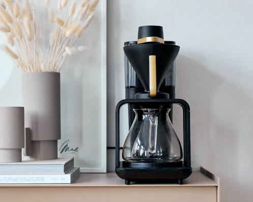 Melitta epour Filterkaffeemaschine mit Glaskanne und goldfarbenem Designelement auf einem Sideboard